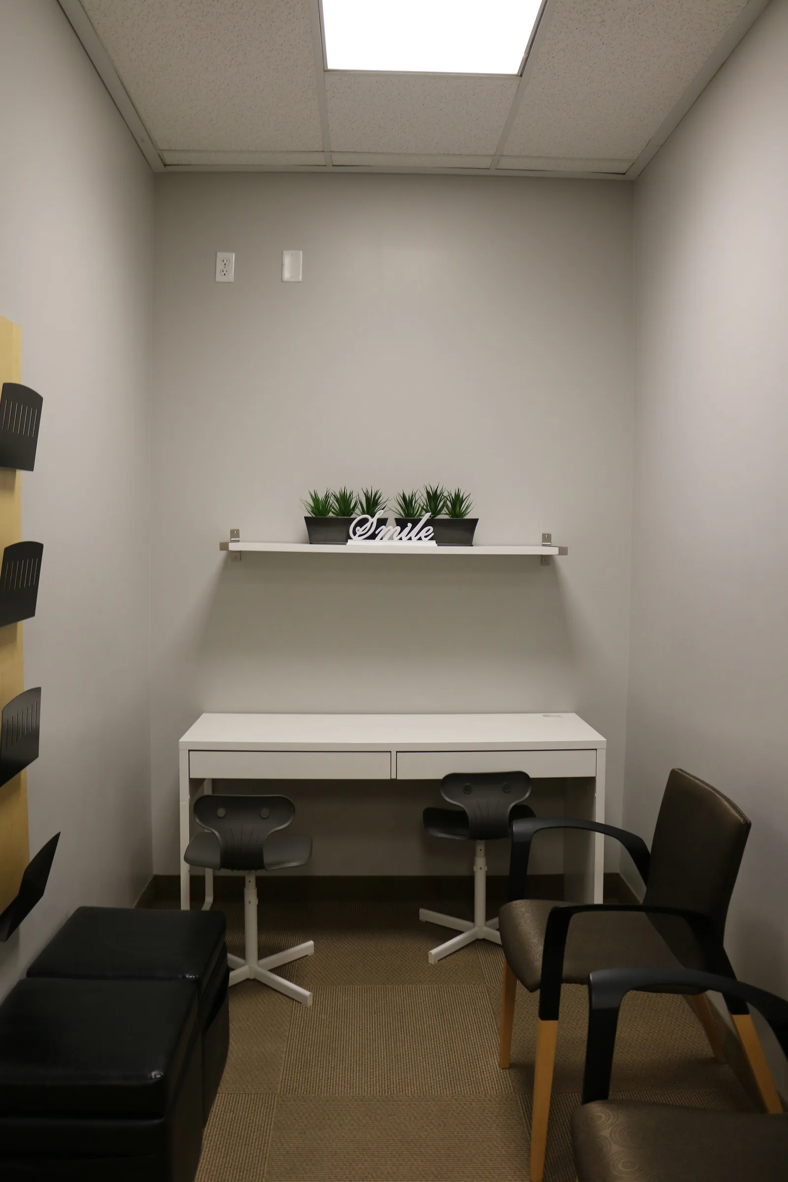 Consultation room with a white desk, office chairs, and a shelf with plants and a decorative "Smile" sign.